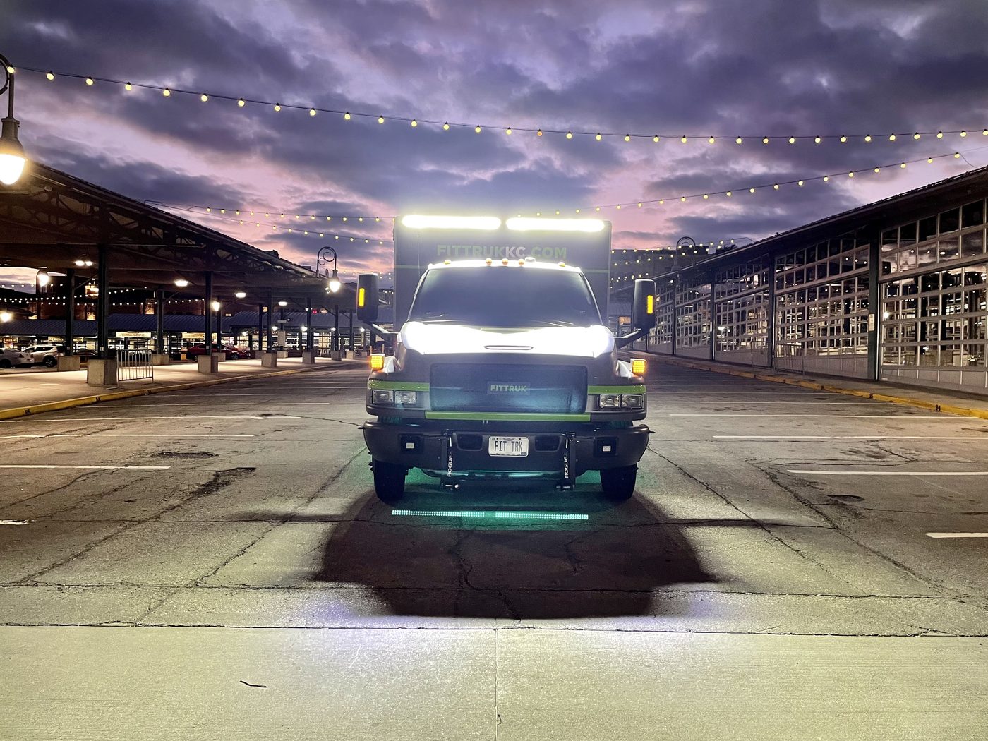 Fit Truk mobile fitness vehicle at dusk, headlights and roof lights on, parked in a paved lot