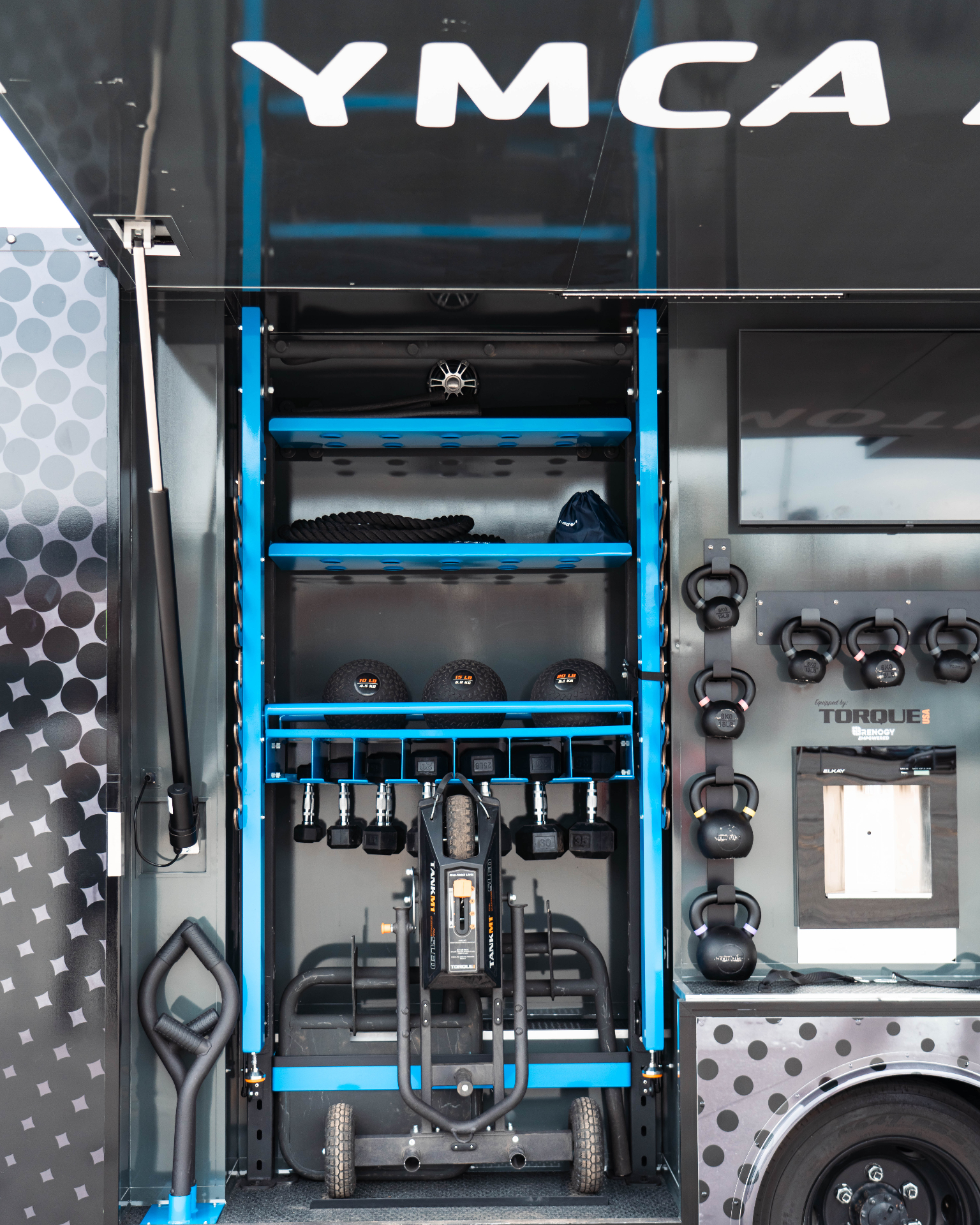 Open equipment compartment showing blue and black storage racks and overhead YMCA branding